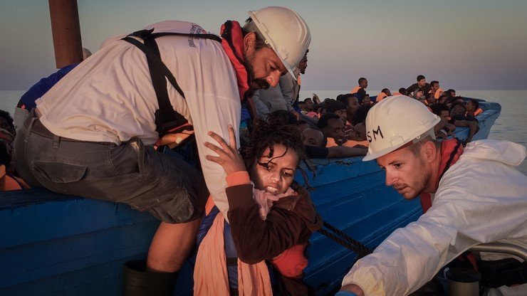 A woman is being helped from a wooden boat carrying around 350 people to an MSF rig that will bring her on board Dignity.